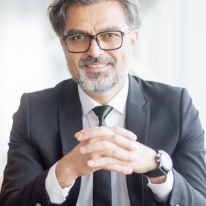 Closeup of Smiling Business Leader Sitting at Table Closeup portrait of smiling middle-aged handsome business man looking at camera and sitting with his hands clasped. Front view.